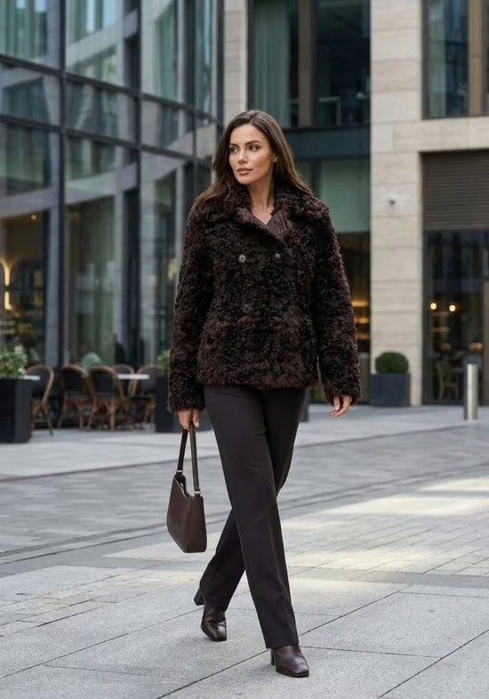 Damen-Curly-Lammfelljacke in Dunkelbraun, im Streetstyle von vorn mit Handtasche getragen.