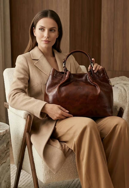 Braune Leder-Handtasche von vorne, vom Model im Sessel gehalten und getragen.