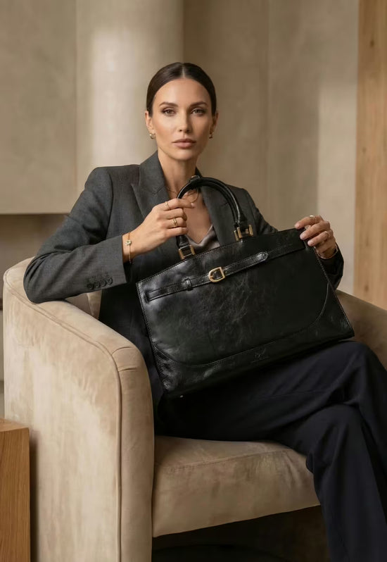 Schwarze Damen-Handtasche aus Leder wird von einer Frau im Sessel getragen