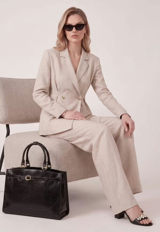 Schwarze Damen-Handtasche aus Leder neben einer sitzenden Frau im hellen Studio