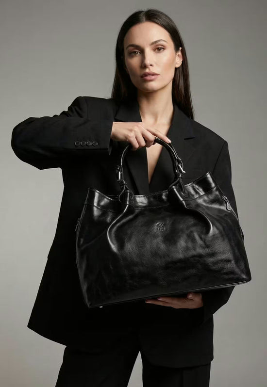 Damen-Handtasche aus Leder in Schwarz, von einer Frau vor dunklem Hintergrund getragen.