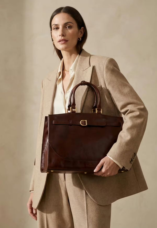 Braune Leder-Hobo-Tasche wird von einer Frau als Schultertasche zum beigen Anzug getragen.