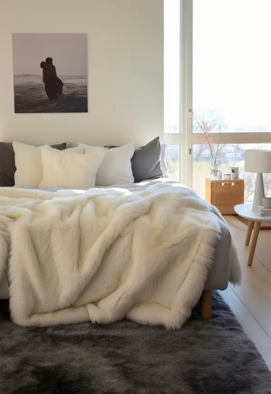 Lammfelldecke aus Lammfell in Naturweiß über das Bett im Schlafzimmer drapiert.
