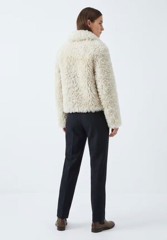 Cremefarbene Curly-Lammfelljacke für Damen in Rückenansicht mit kurzem Schnitt und flauschiger Oberfläche