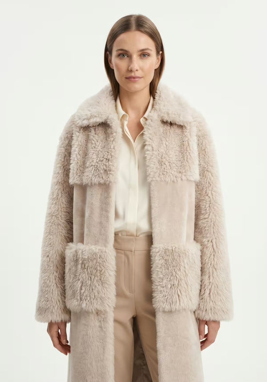 Beiger Lammfellmantel für Damen am Modell mit sichtbaren Fellpartien, Hemd und Hose darunter.