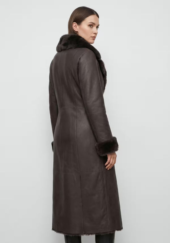 Brauner Lammfellmantel für Damen am Model von hinten mit geradem Schnitt und hohem Pelzkragen.