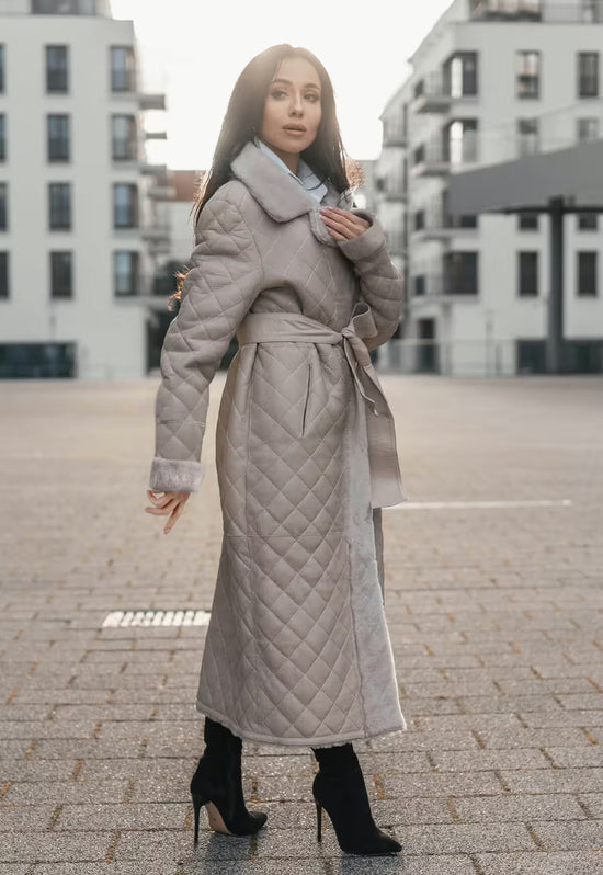 Damen-Lammfellmantel in Beige von hinten in Dreiviertelansicht, mit Gürtel und Lammfellbesatz.
