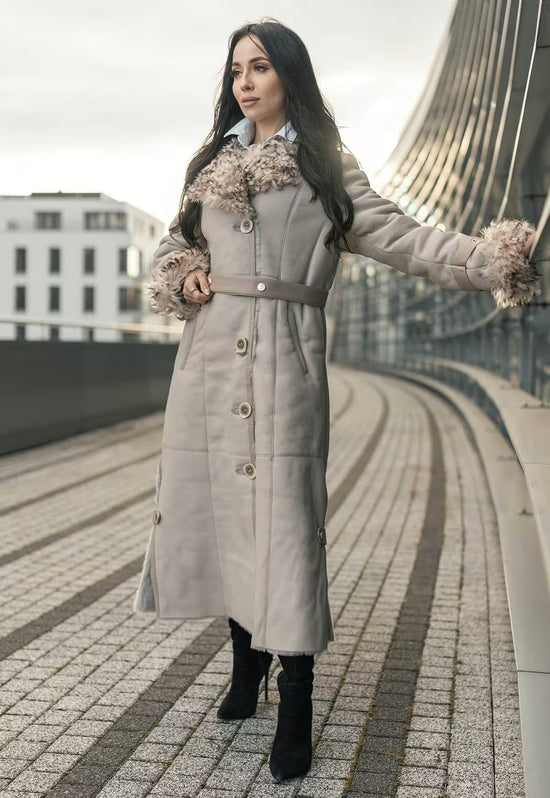 Lammfellmantel für Damen in Beige in Seitenansicht, mit großem Fellkragen, Gürtel und langem Schnitt.