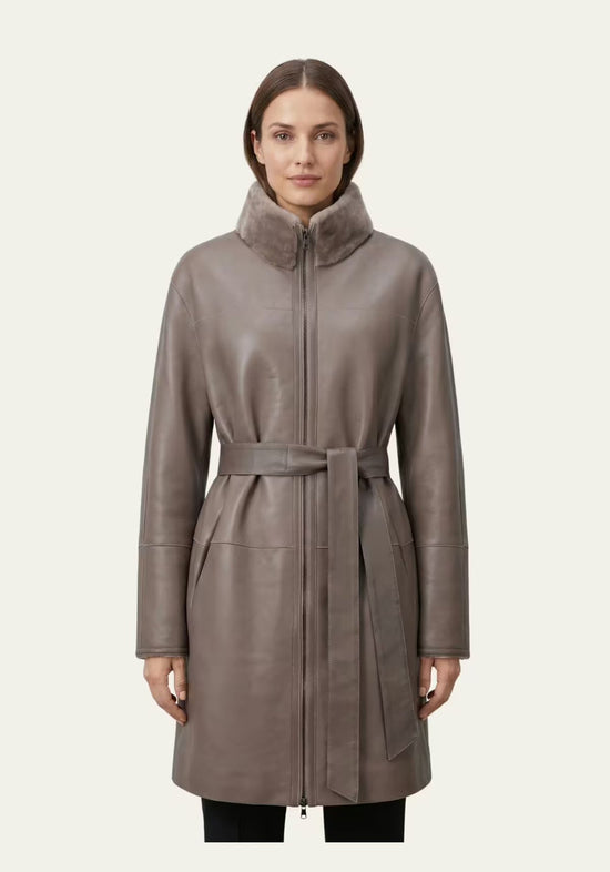 Graubrauner Damen-Lammfellmantel aus Merino Shearling, getragen von vorn mit Reißverschluss und Bindegürtel.