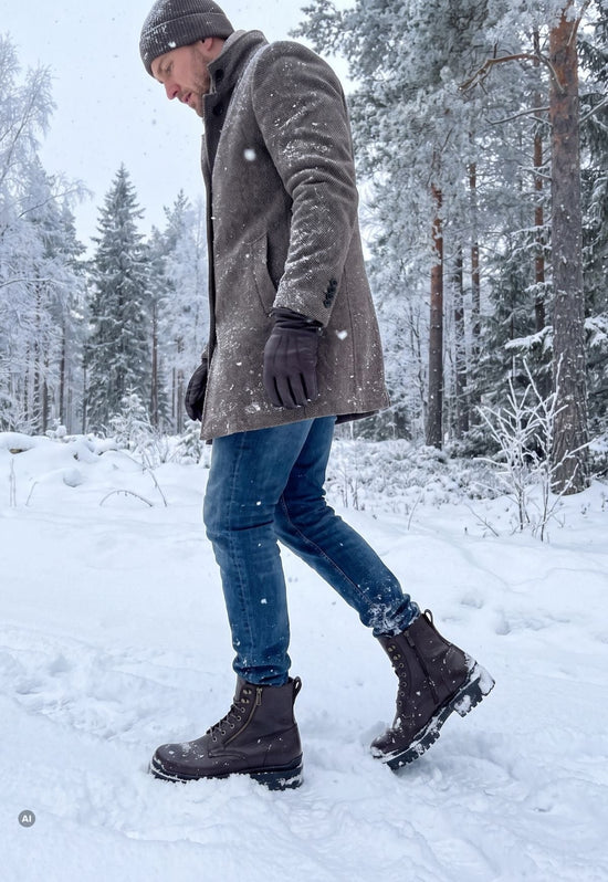 Dunkelbraune Herren-Lammfell-Stiefelette aus Leder im Schnee, getragen zu Mantel und Jeans.