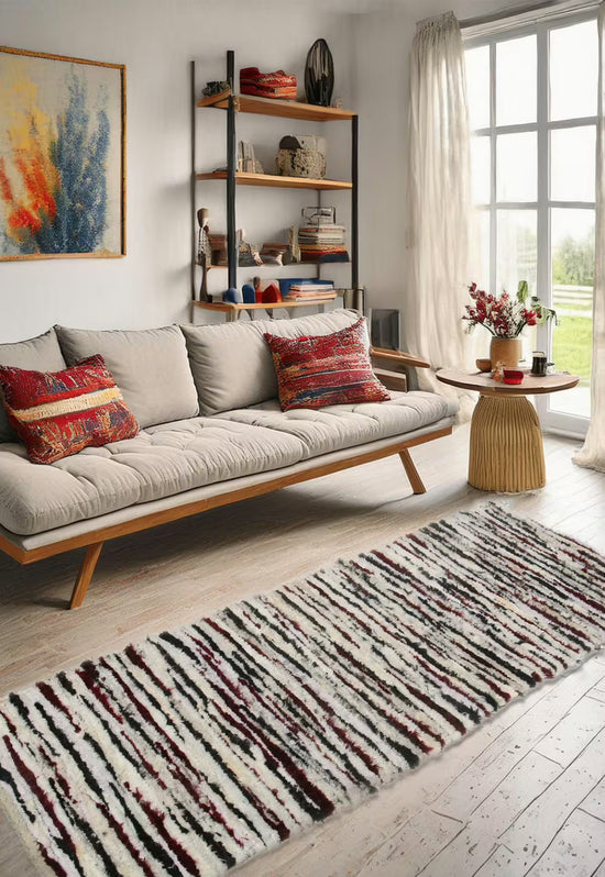 Schafwoll-Teppich in Mehrfarbig im hellen Wohnzimmer vor Sofa, Regal und Fenster