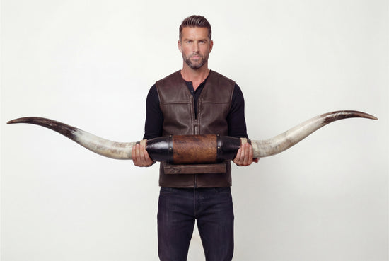 Mann hält eine schwarze Wanddekoration aus Leder mit langen Longhorns von vorne.