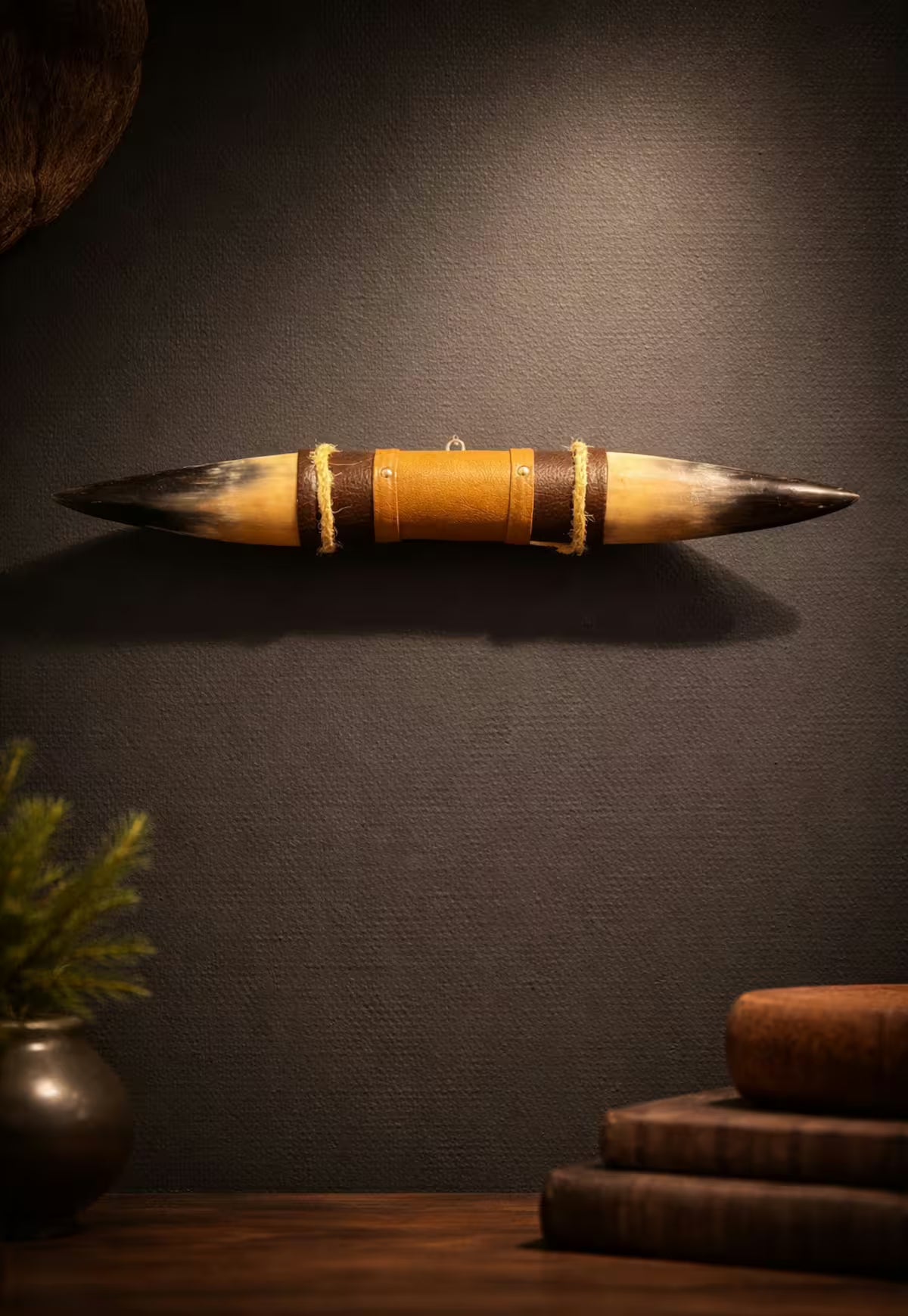 Wanddekoration aus Naturhorn mit Leder-Holzhalterung an dunkler Wand, frontal inszeniert.